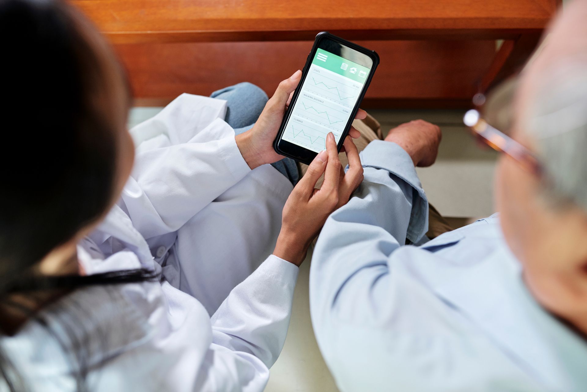 A doctor and a patient are sitting on the floor looking at a cell phone.