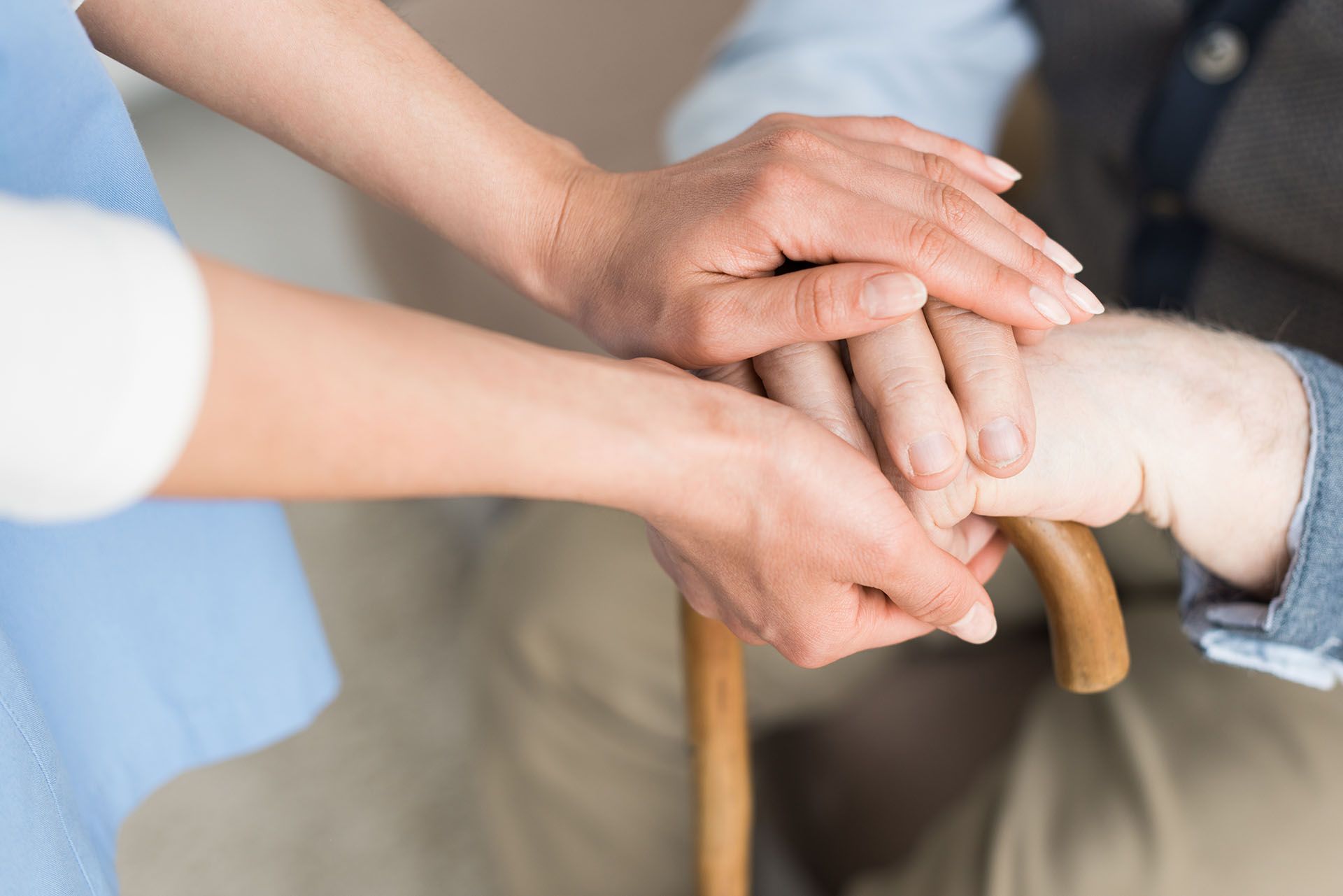 A woman is holding the hand of an elderly man with a cane.