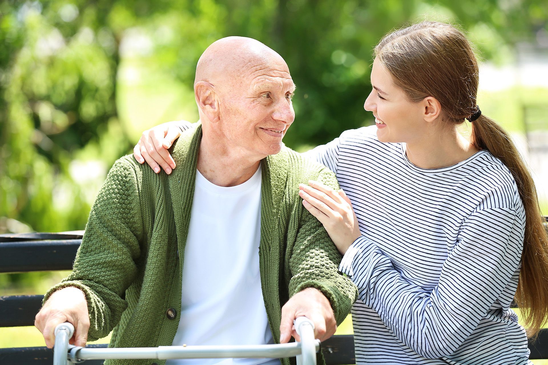 An elderly man with a walker is sitting on a bench with a woman.