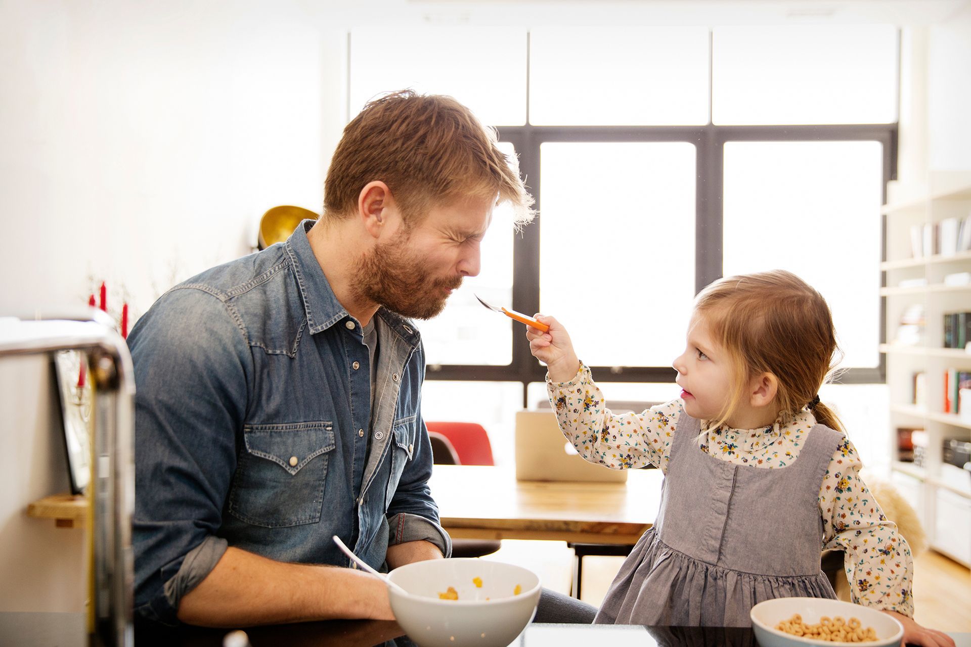 A father and daughter are sitting at a table eating cereal.