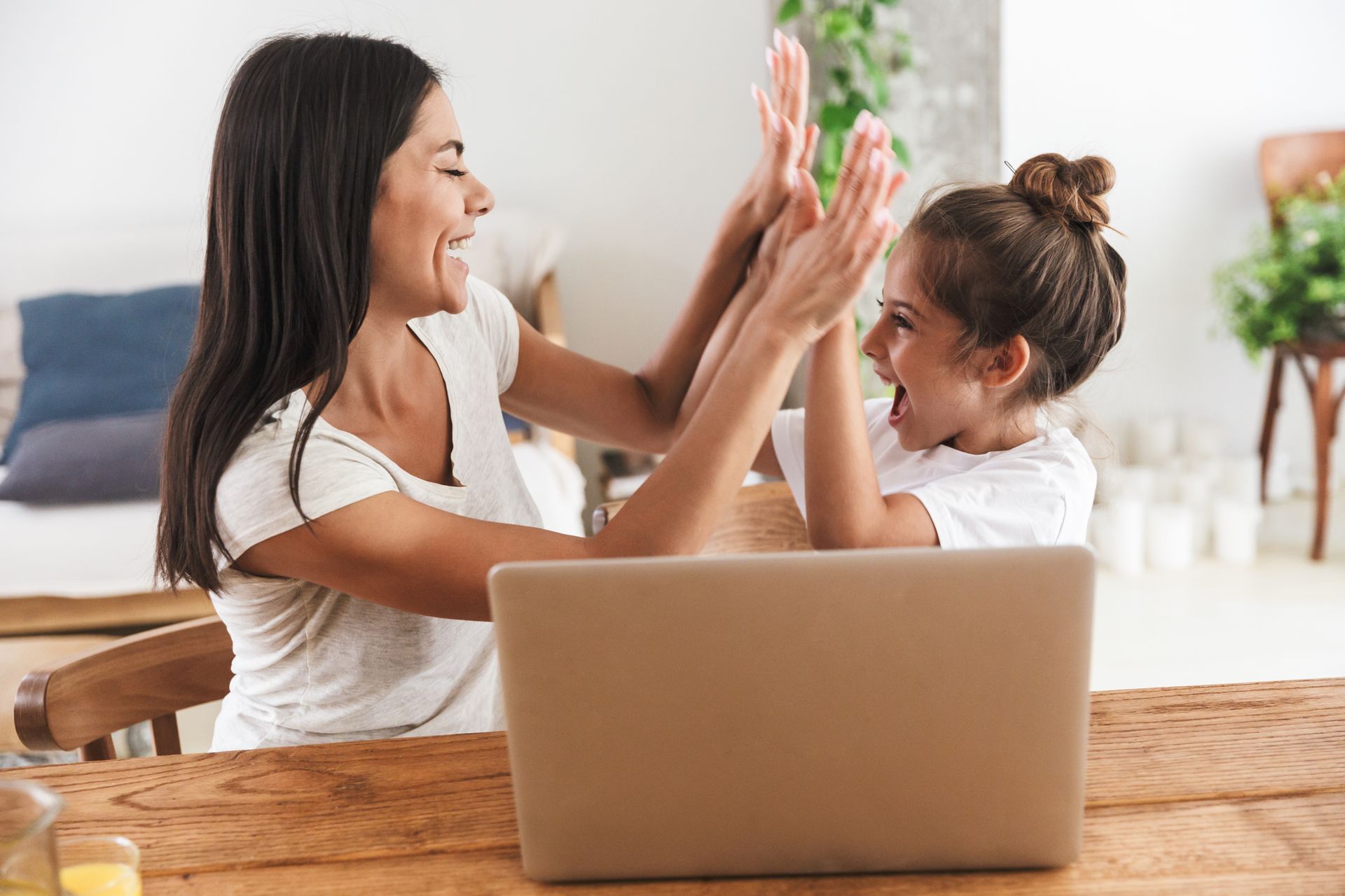 a woman and a little girl are giving each other a high five while sitting at a table with a laptop
