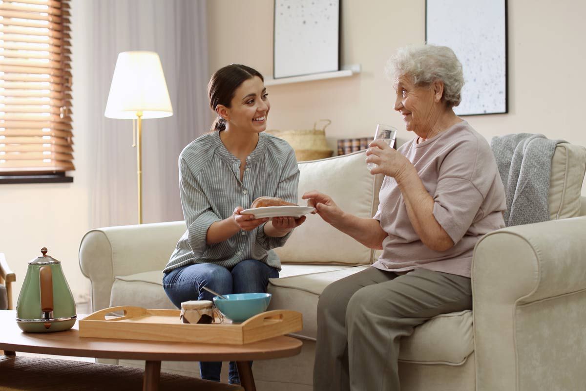 a woman is giving an elderly woman food while they are sitting on a couch