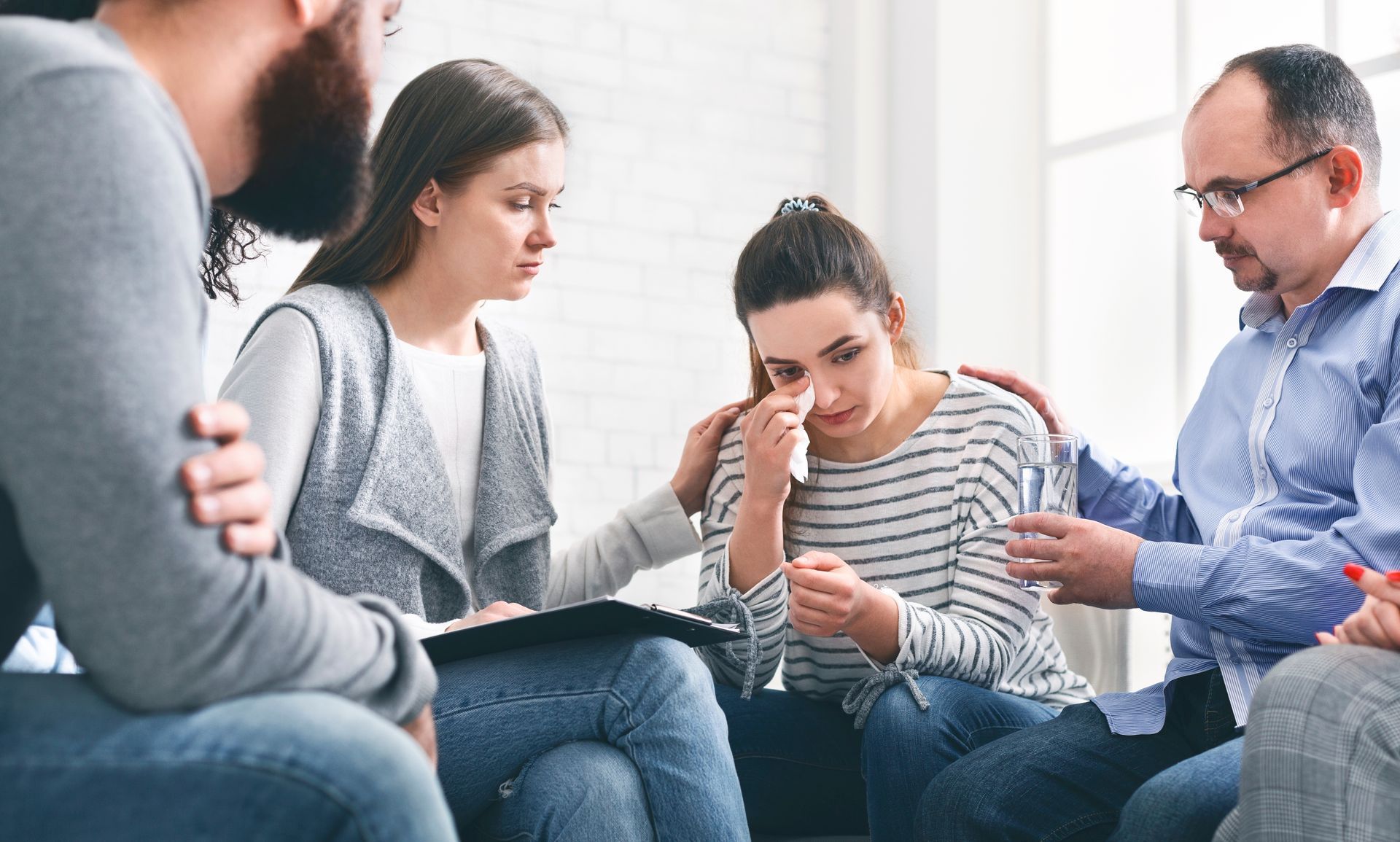 A group of people are sitting around a woman who is crying.