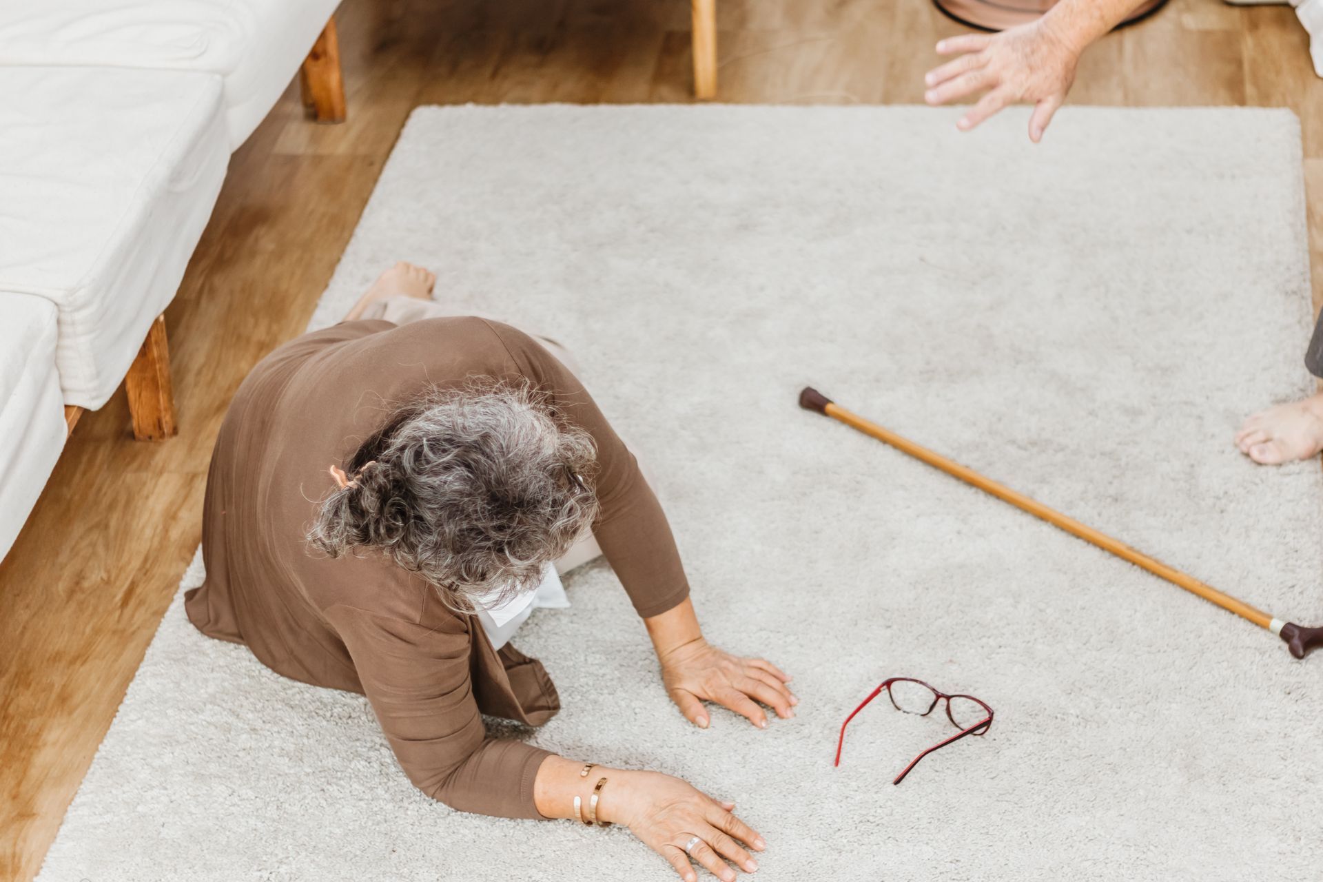 An elderly woman is lying on the floor with a cane.