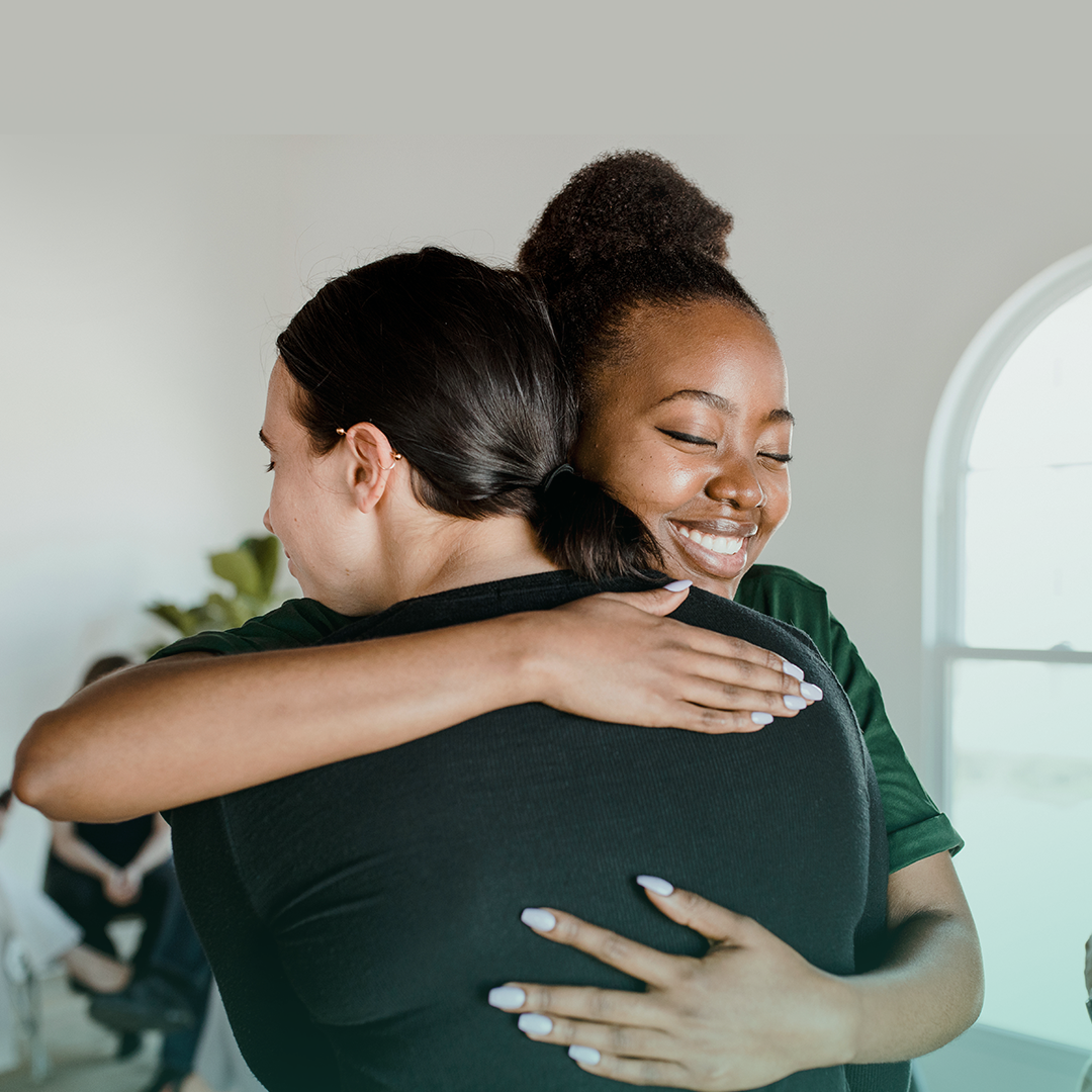 Two women are hugging each other in a room.