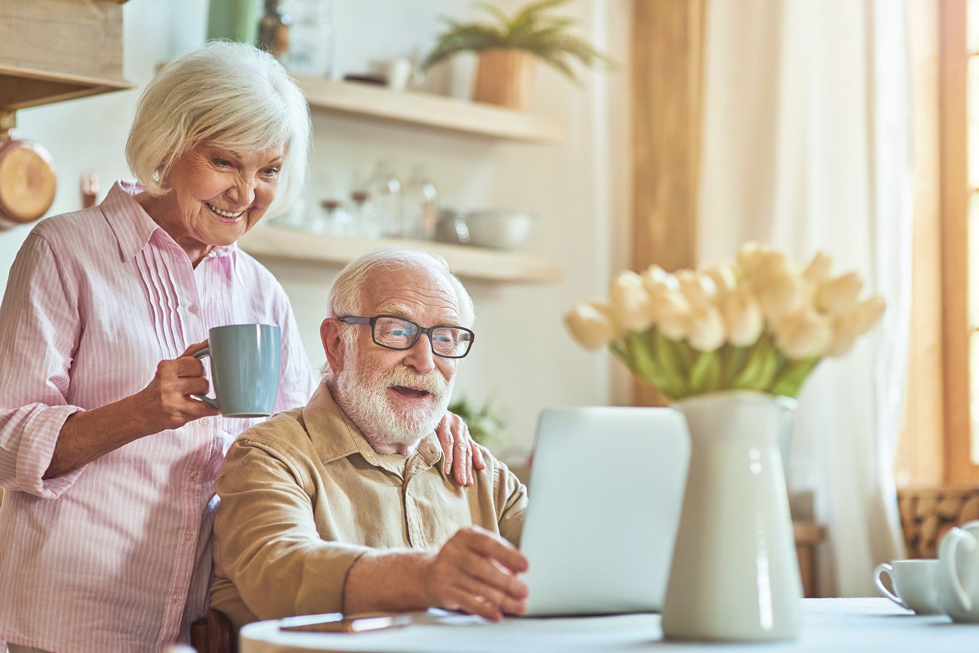 An elderly couple is sitting at a table using a laptop computer.