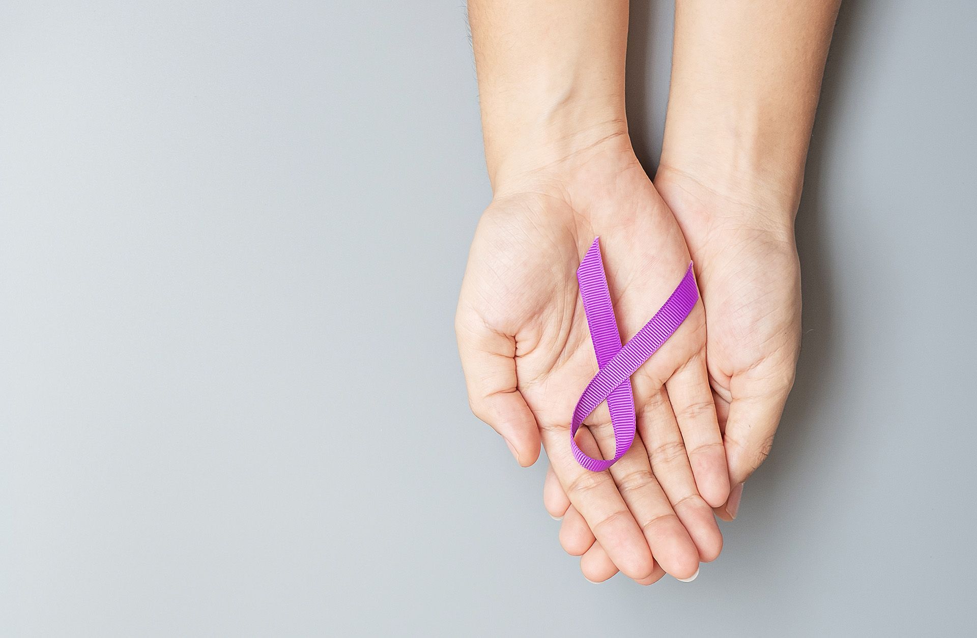 A person is holding a purple ribbon in their hands.