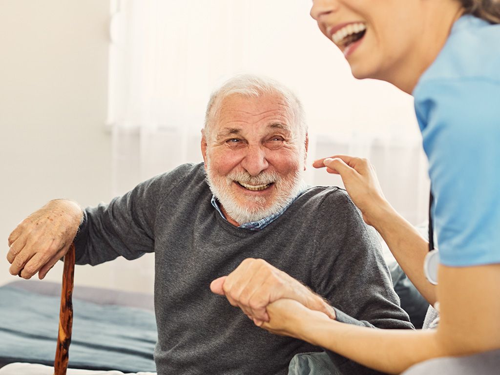 A nurse is holding the hand of an elderly man with a cane.