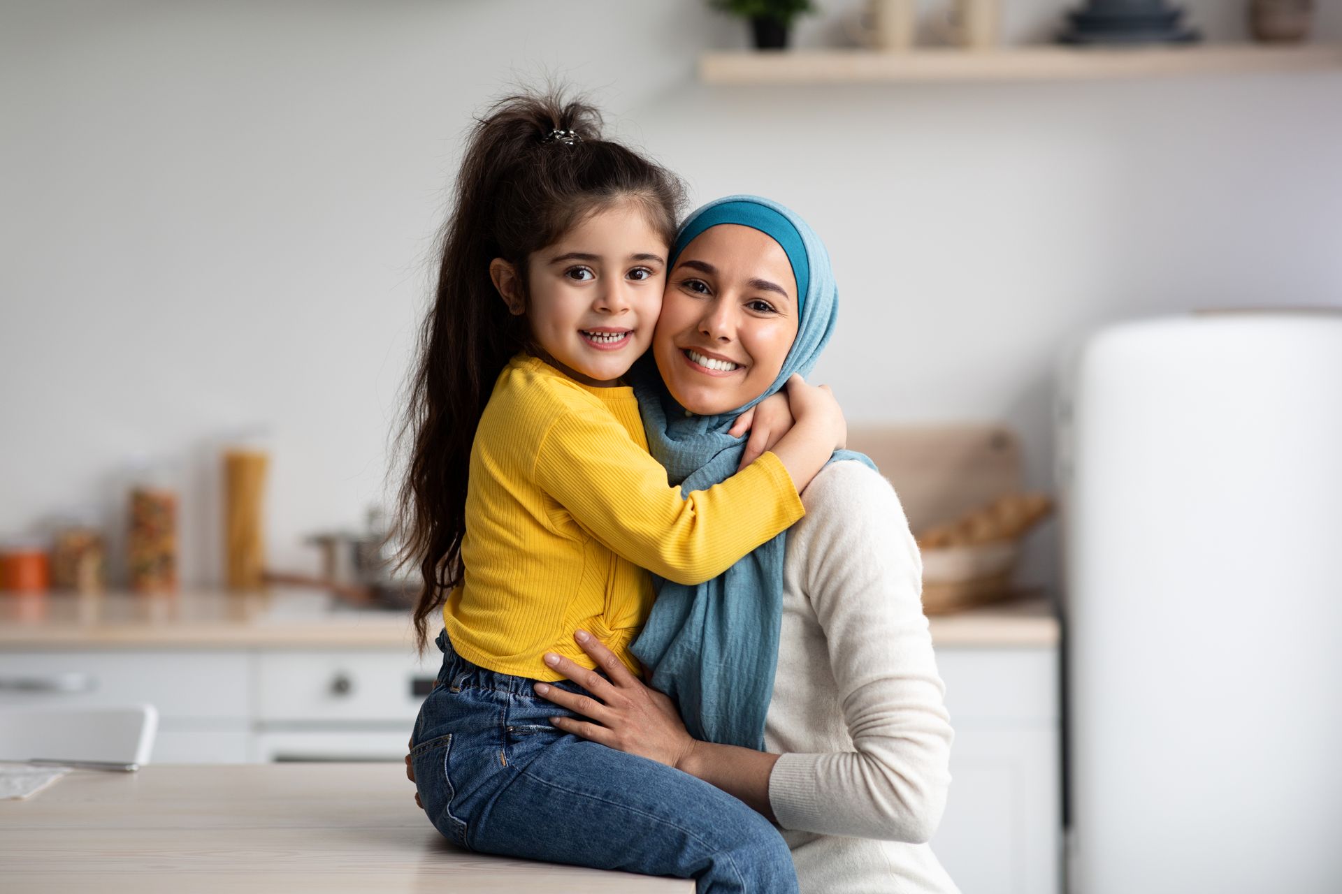 a woman in a hijab is hugging a little girl in a kitchen
