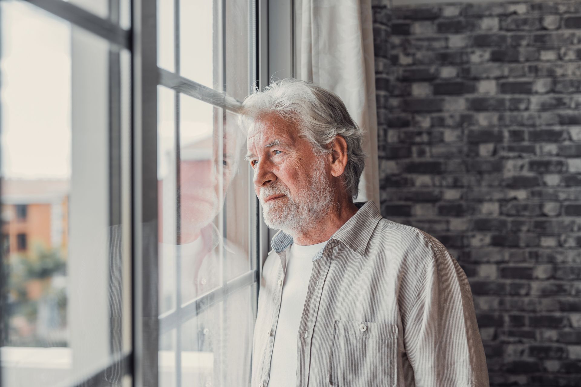 An elderly man is looking out of a window.