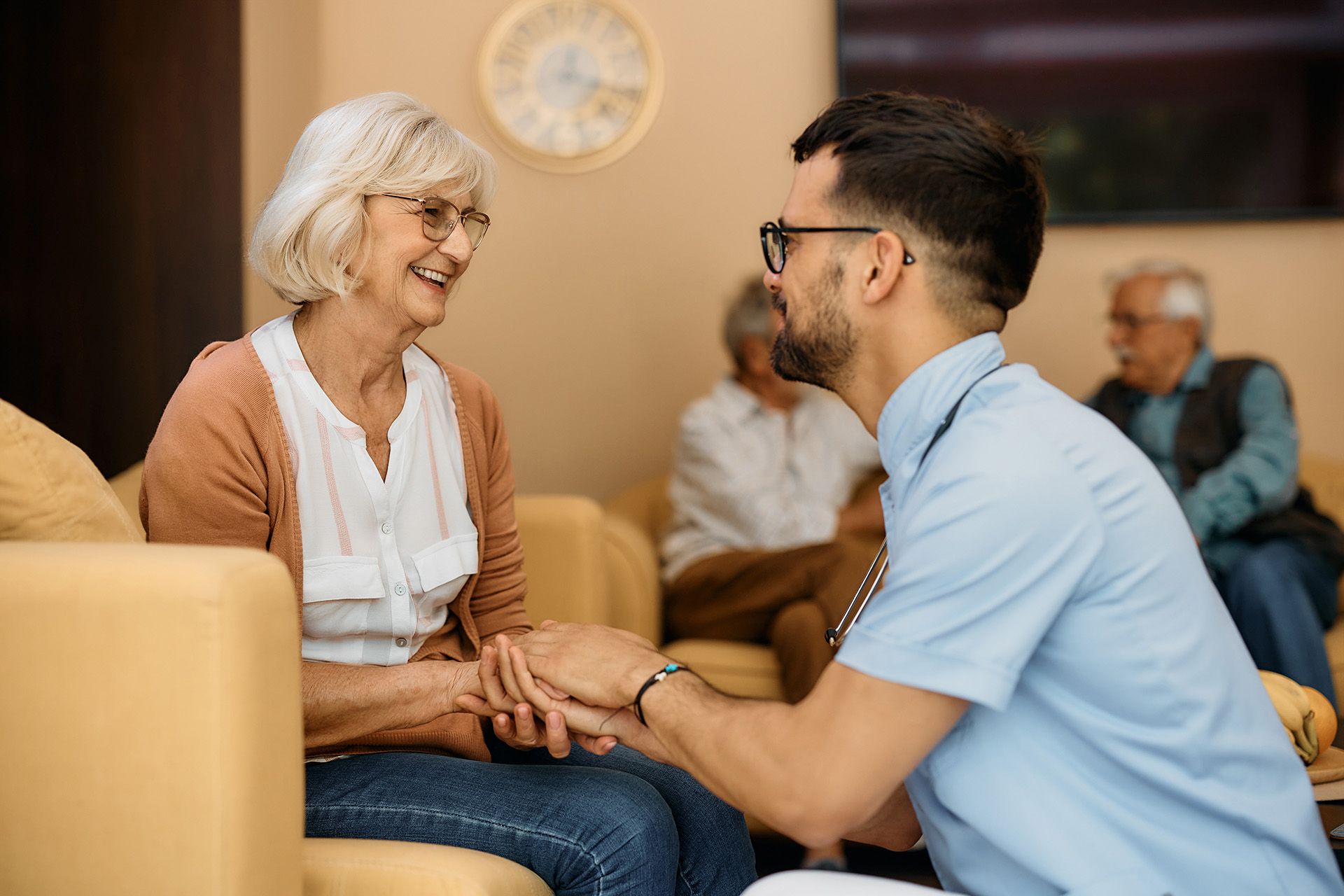 A man is holding the hand of an elderly woman in a nursing home.