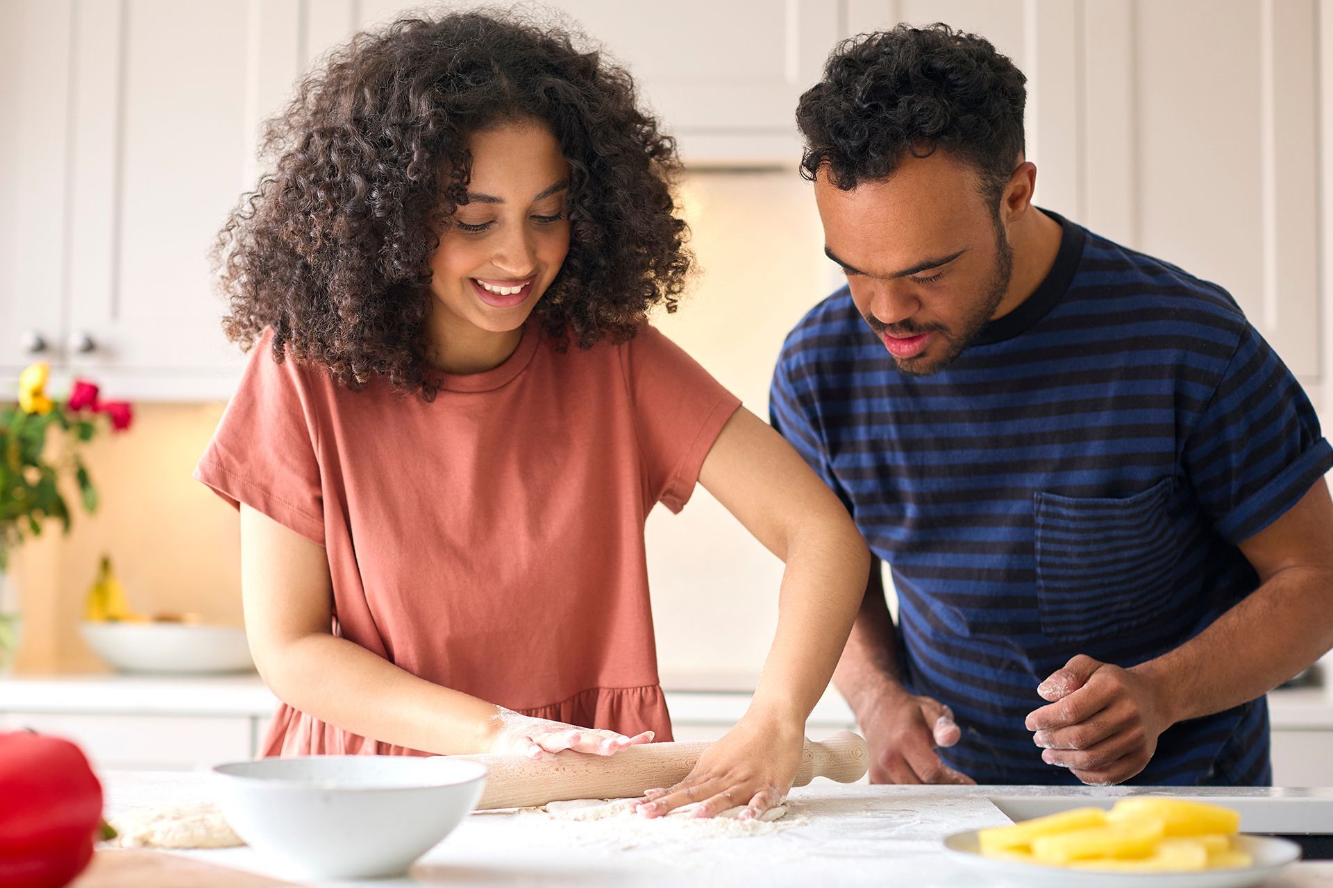 a man and a woman are rolling dough together in a kitchen