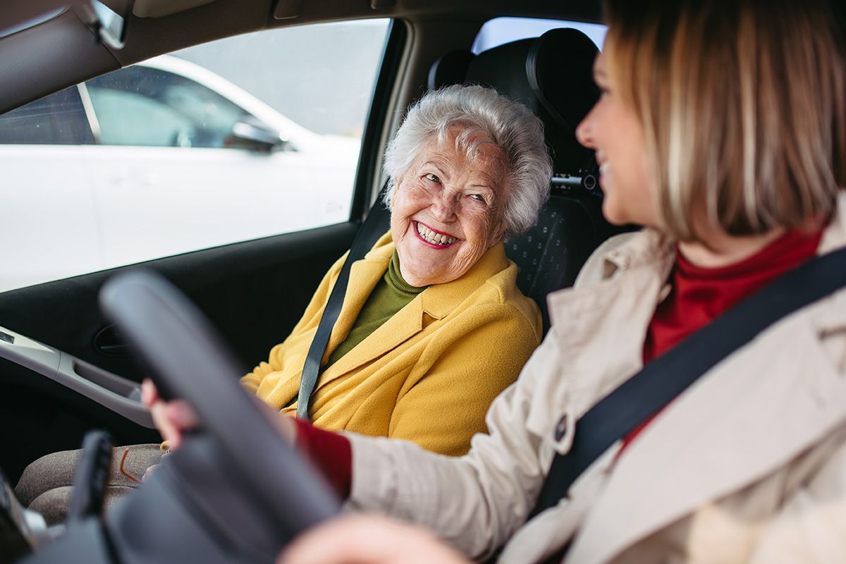 A woman is driving a car with an elderly woman in the passenger seat.