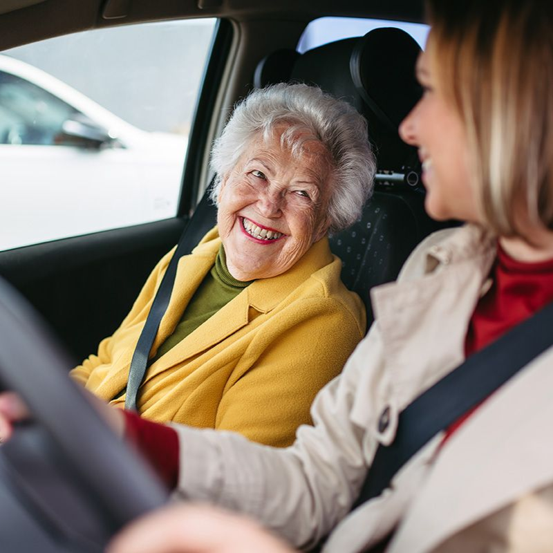 A woman is driving a car with an elderly woman in the passenger seat.