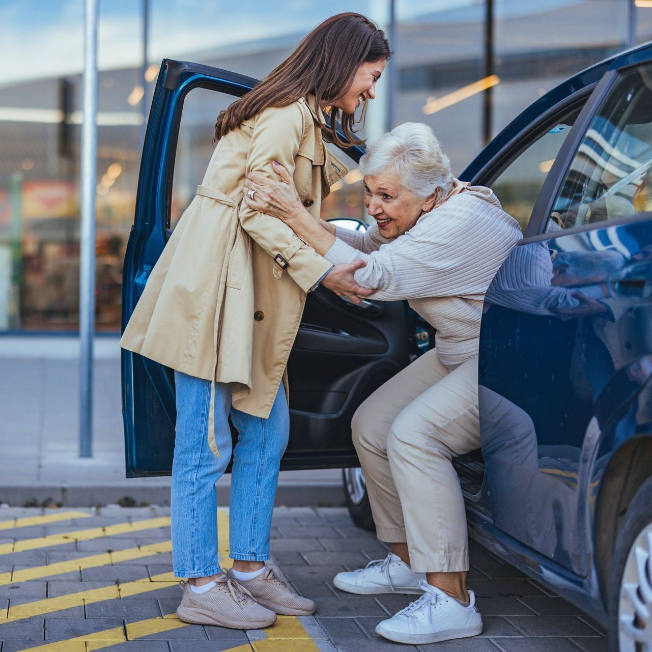 A young woman is helping an older woman get out of a car.