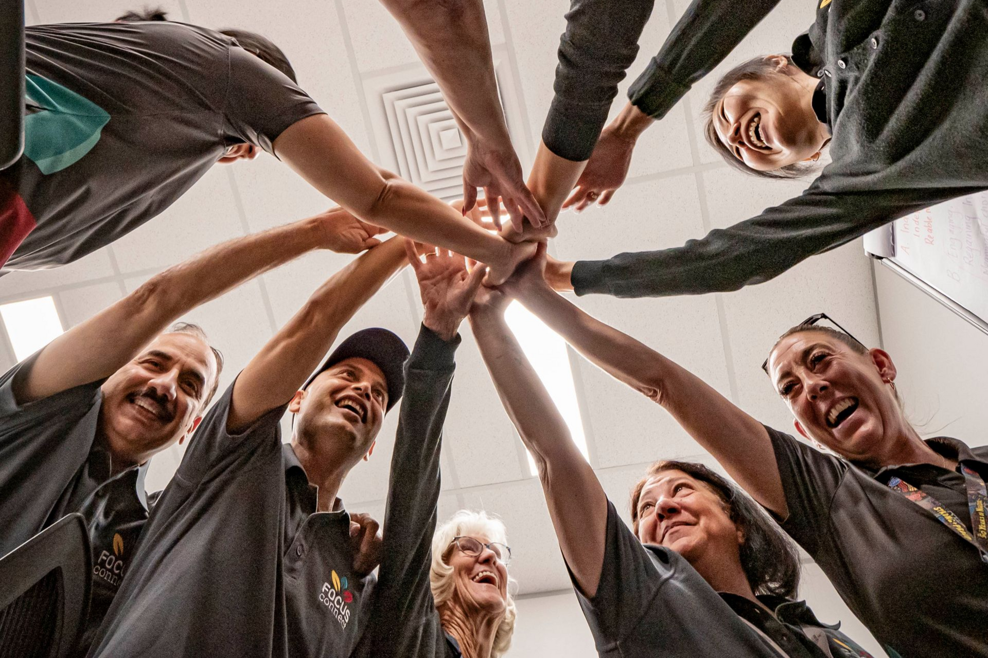 Group of people with hands in a circle, smiling, celebrating success, indoors.