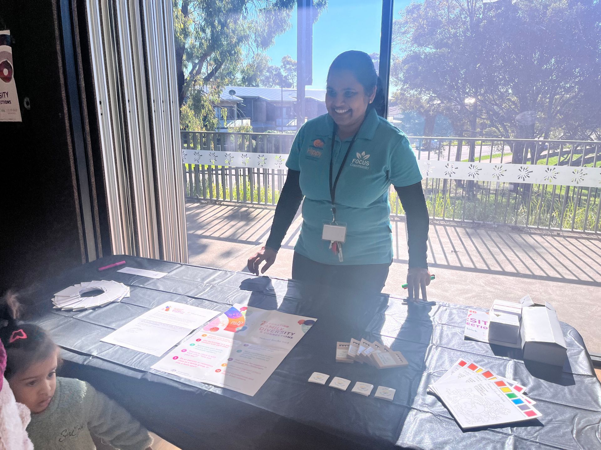 a woman in a green shirt standing behind a table with papers on it