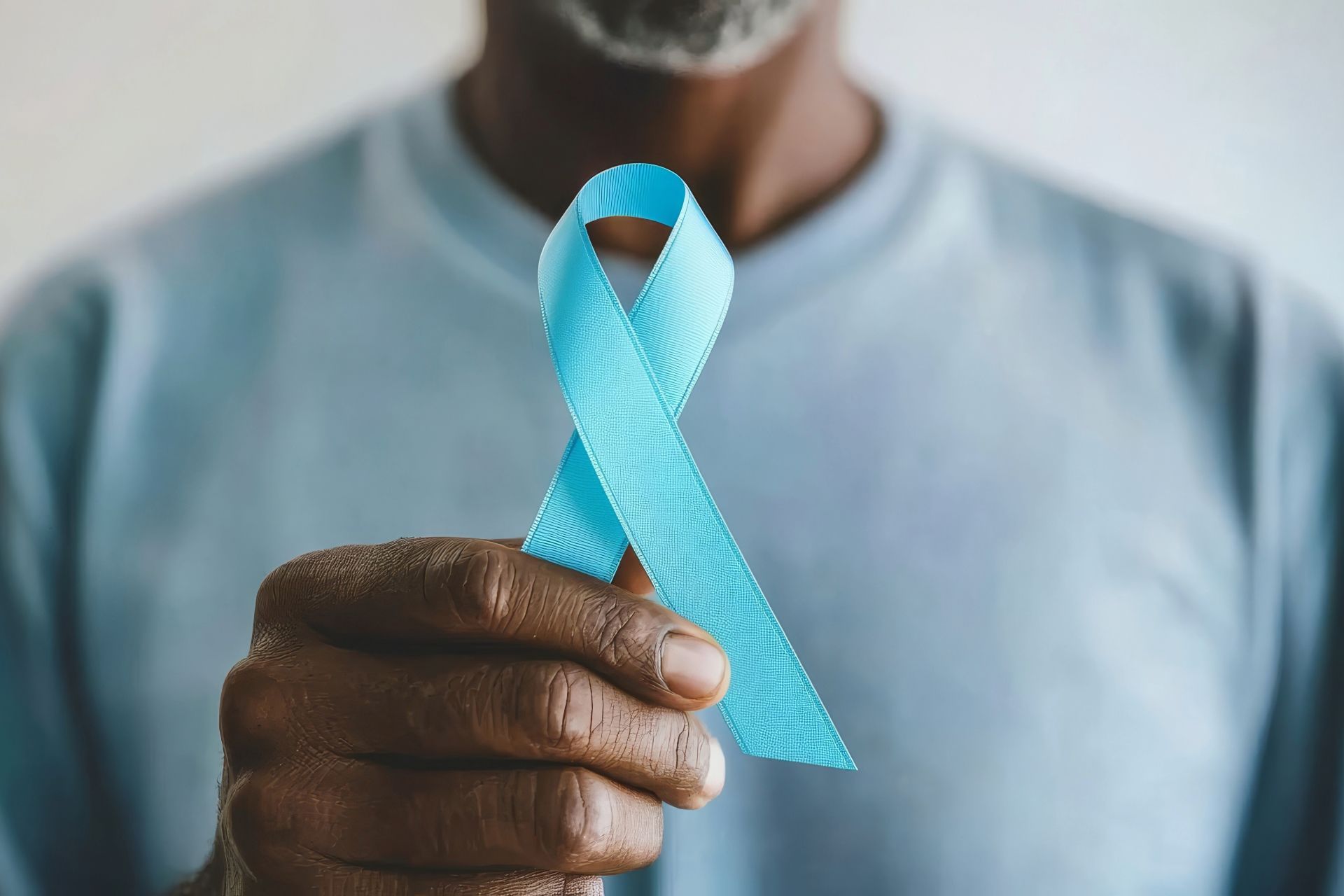 A man is holding a blue ribbon in his hand, Prostate Cancer symbol.