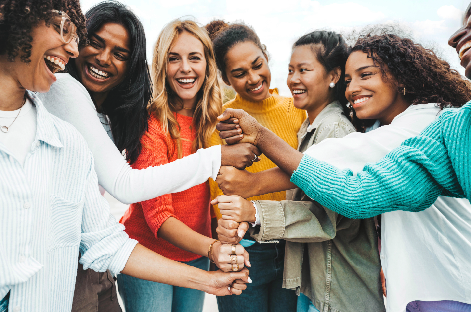 A group of people standing in a circle with their fists stacked on top of each other, smiling and laughing together.