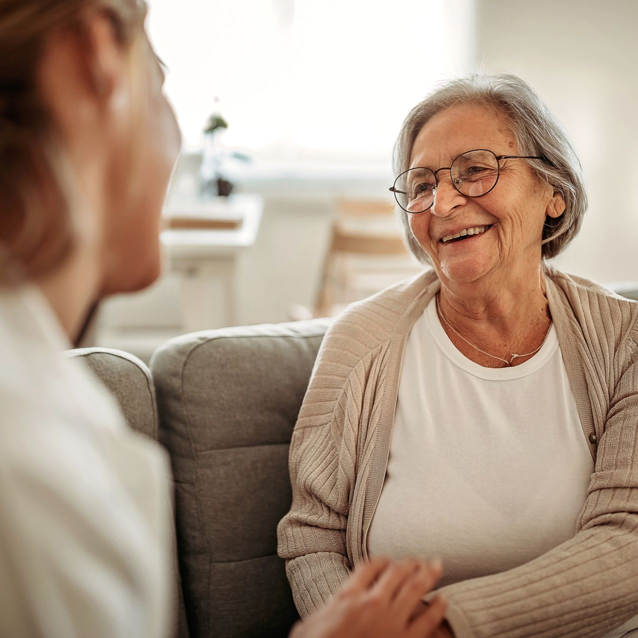 Elderly couple laughing outside, wearing glasses. Man has a white beard. Woman has silver hair.