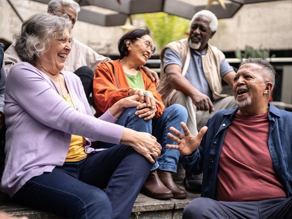A group of older people are sitting on steps laughing.