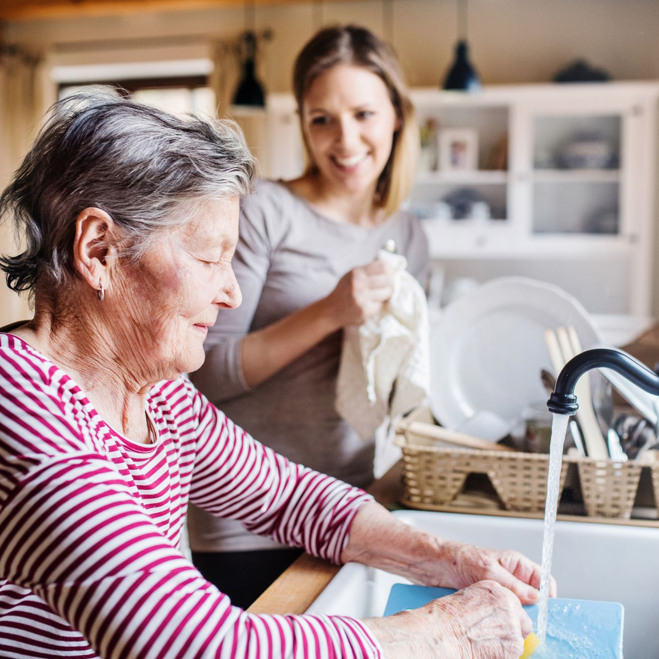 Woman washing dishes at a kitchen sink, another woman drying them.