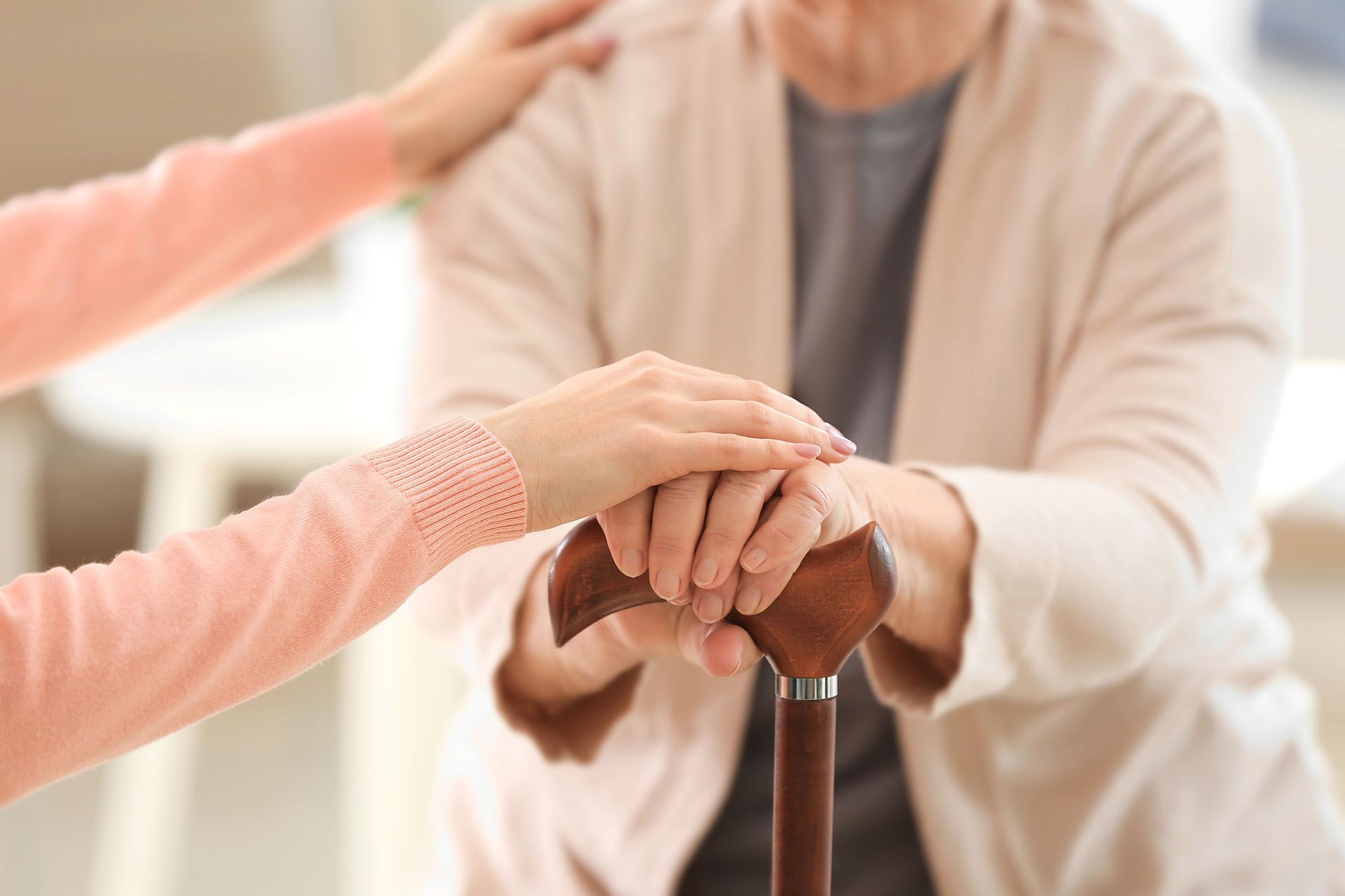 A woman is holding the hand of an elderly woman with a cane.