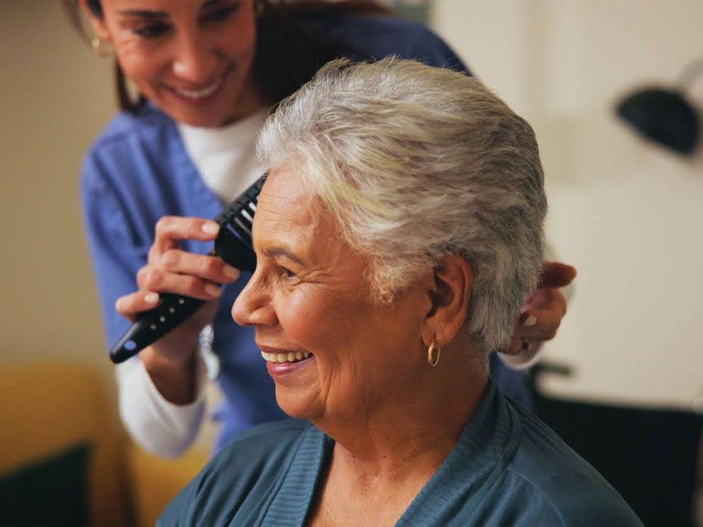 An elderly woman is getting her hair cut by a nurse.