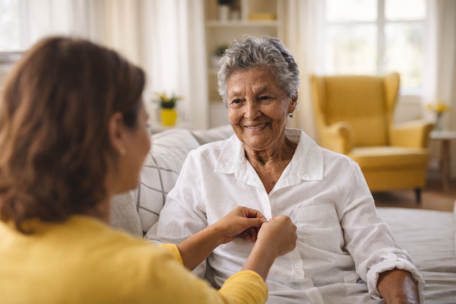 Woman buttoning a senior's shirt in a living room.