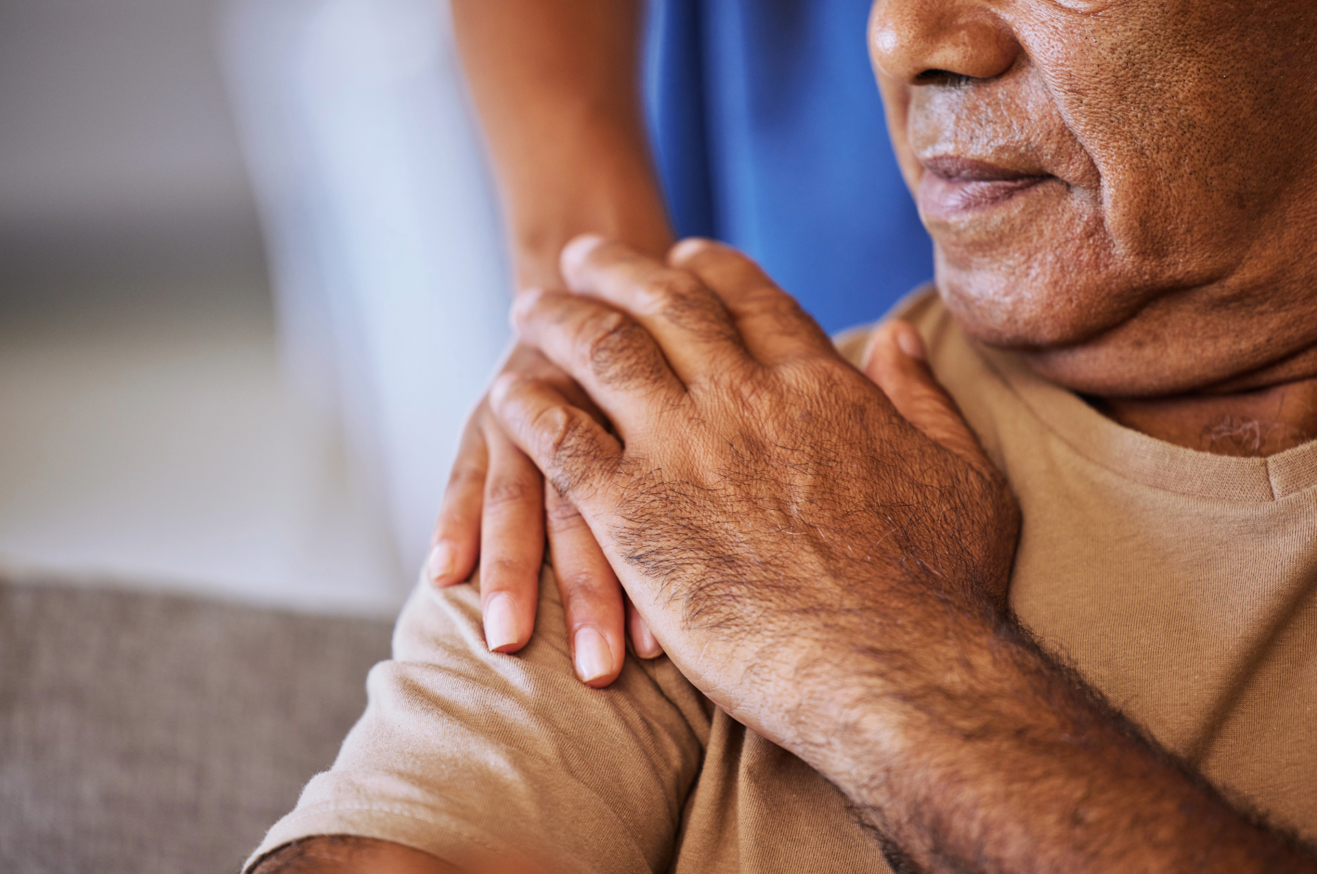 Person with hands clasped, being comforted by another person's hands on their shoulders.