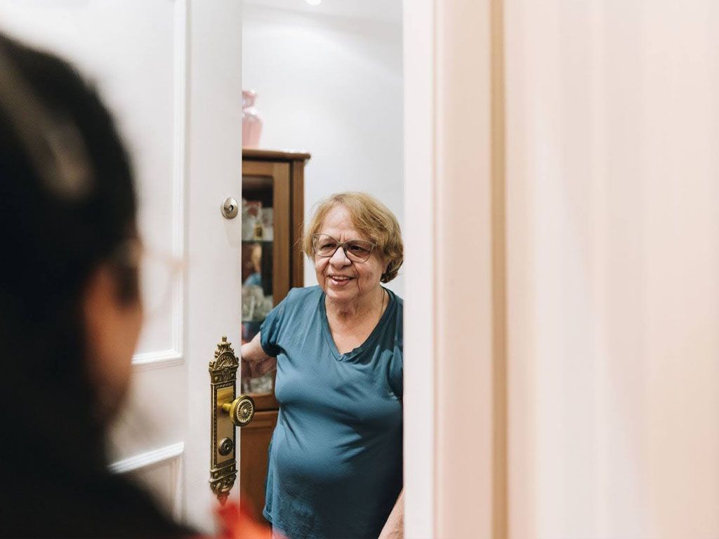 An elderly woman is standing in a doorway talking to a man.