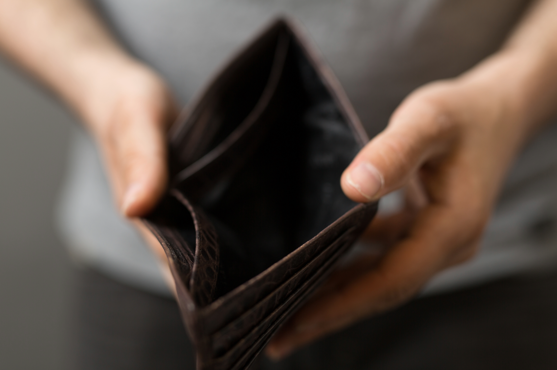 Person holding an empty brown wallet; a sign of financial hardship.