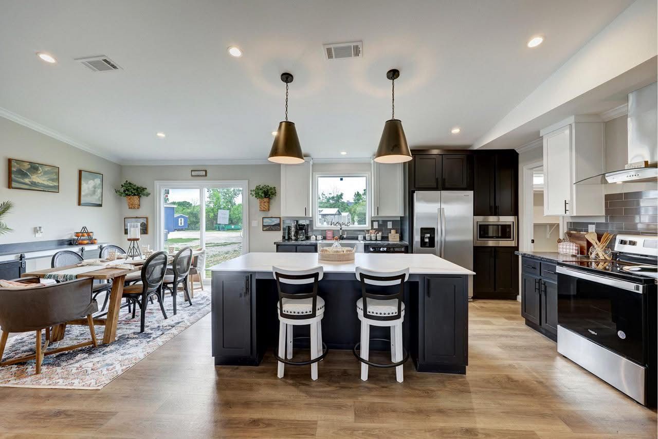 Bright open kitchen and dining area with island, black cabinets, pendant lights, and wood floors