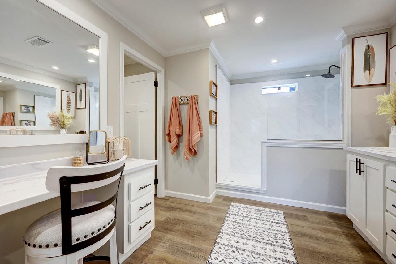 Bright bathroom vanity with chair, drawers, towels, and a frosted glass shower enclosure.