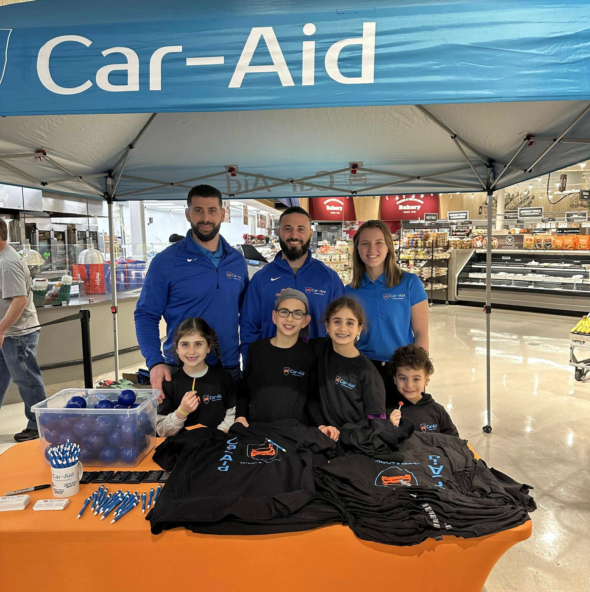 A group of people are standing under a car-aid tent in a store.