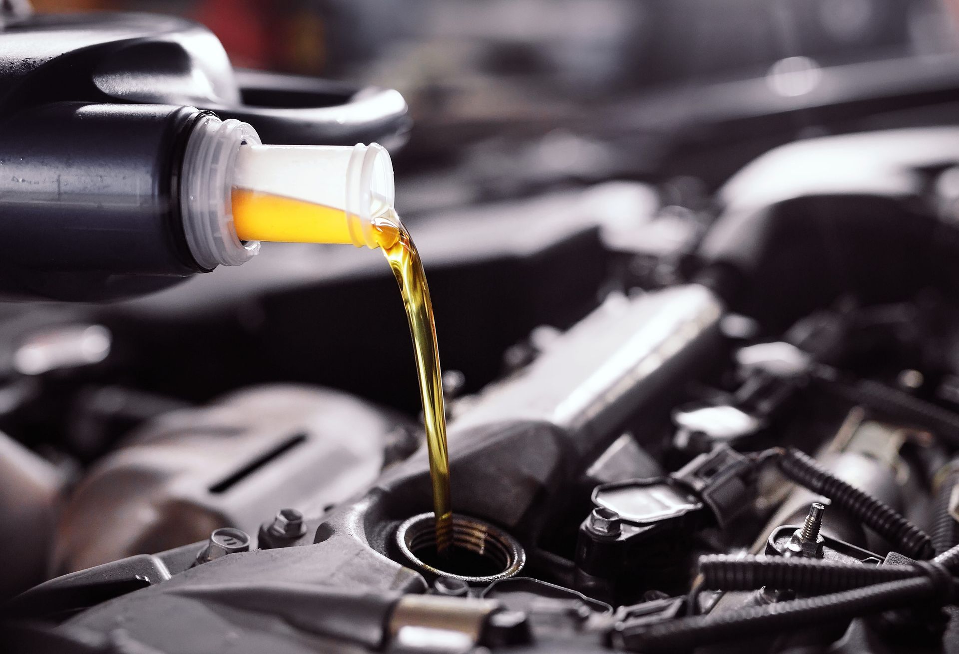 Pouring fresh oil into a car engine. A black bottle dispenses yellow liquid into an engine bay.