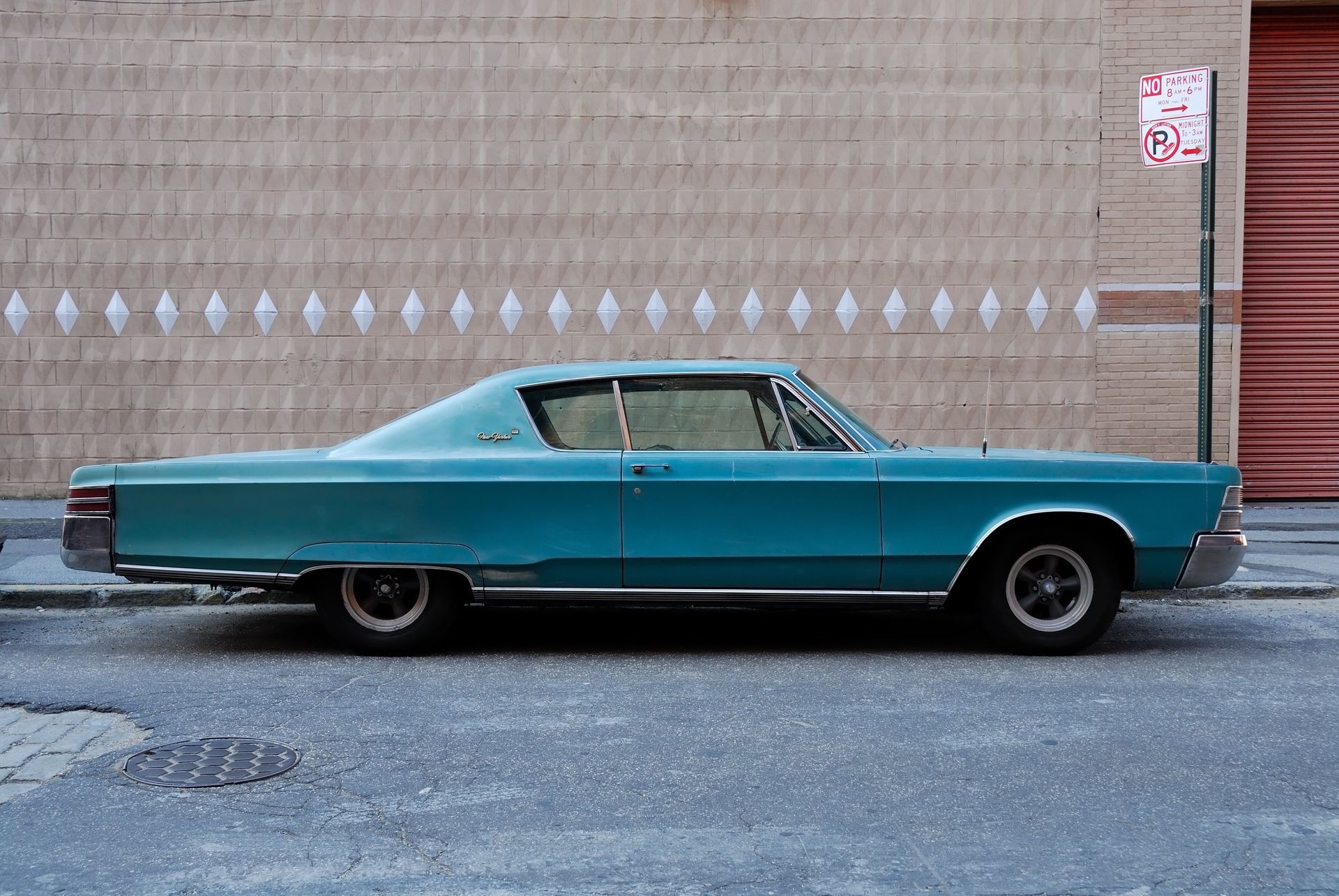 Turquoise vintage car parked on a city street, beside a tan brick wall.