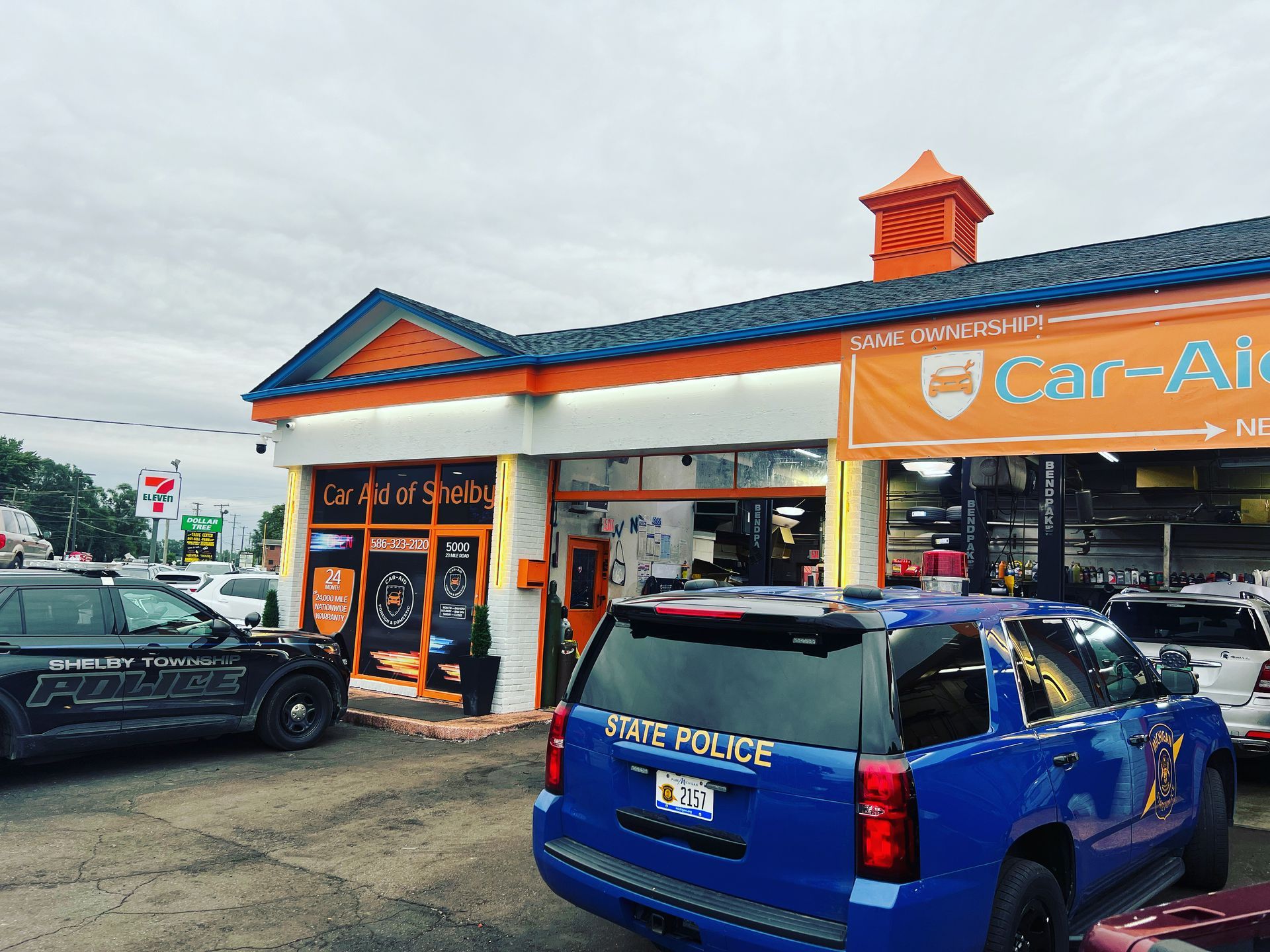 A blue police car is parked in front of a car dealership.