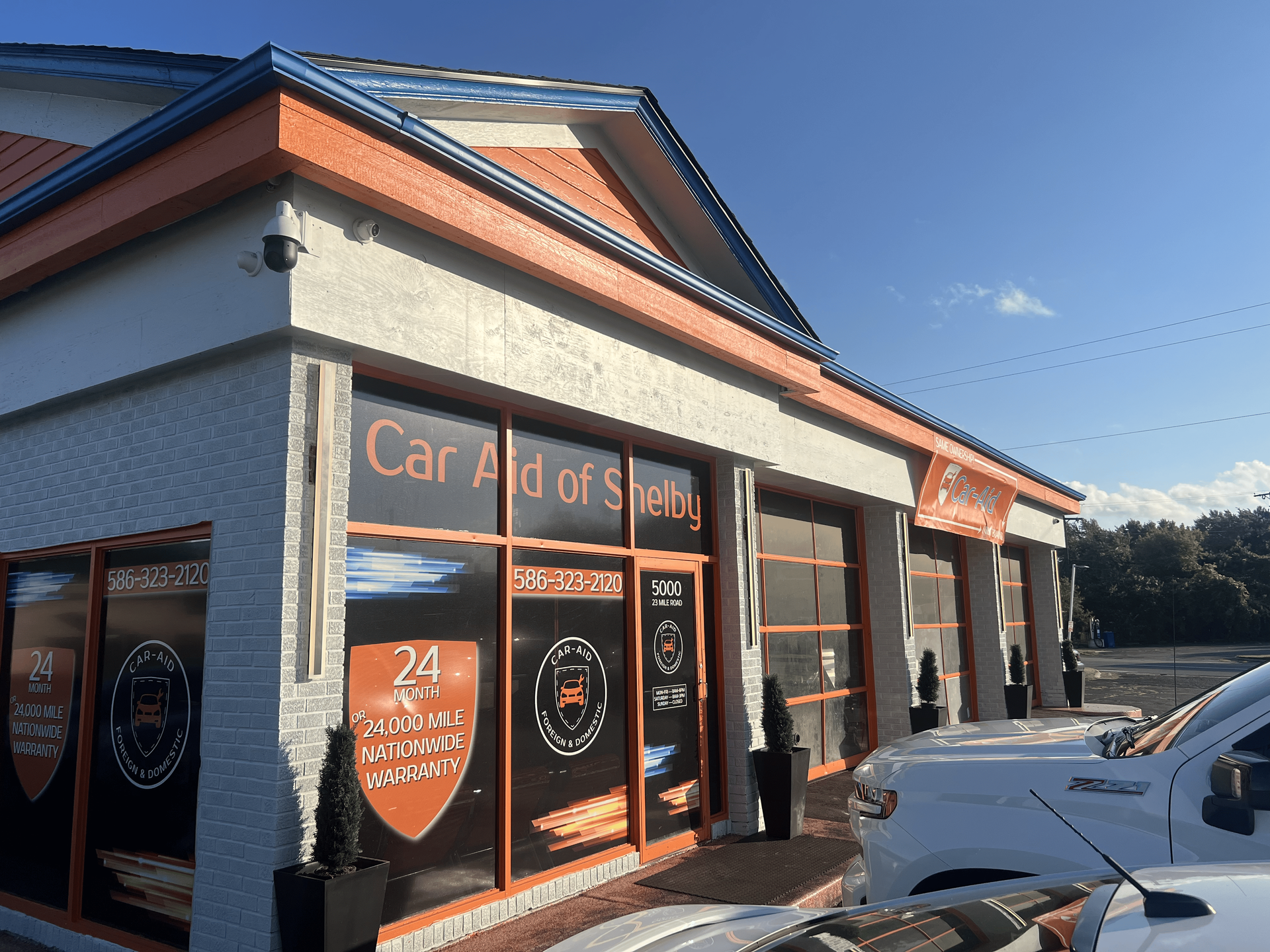 A white truck is parked in front of a building that says car aid of sheds