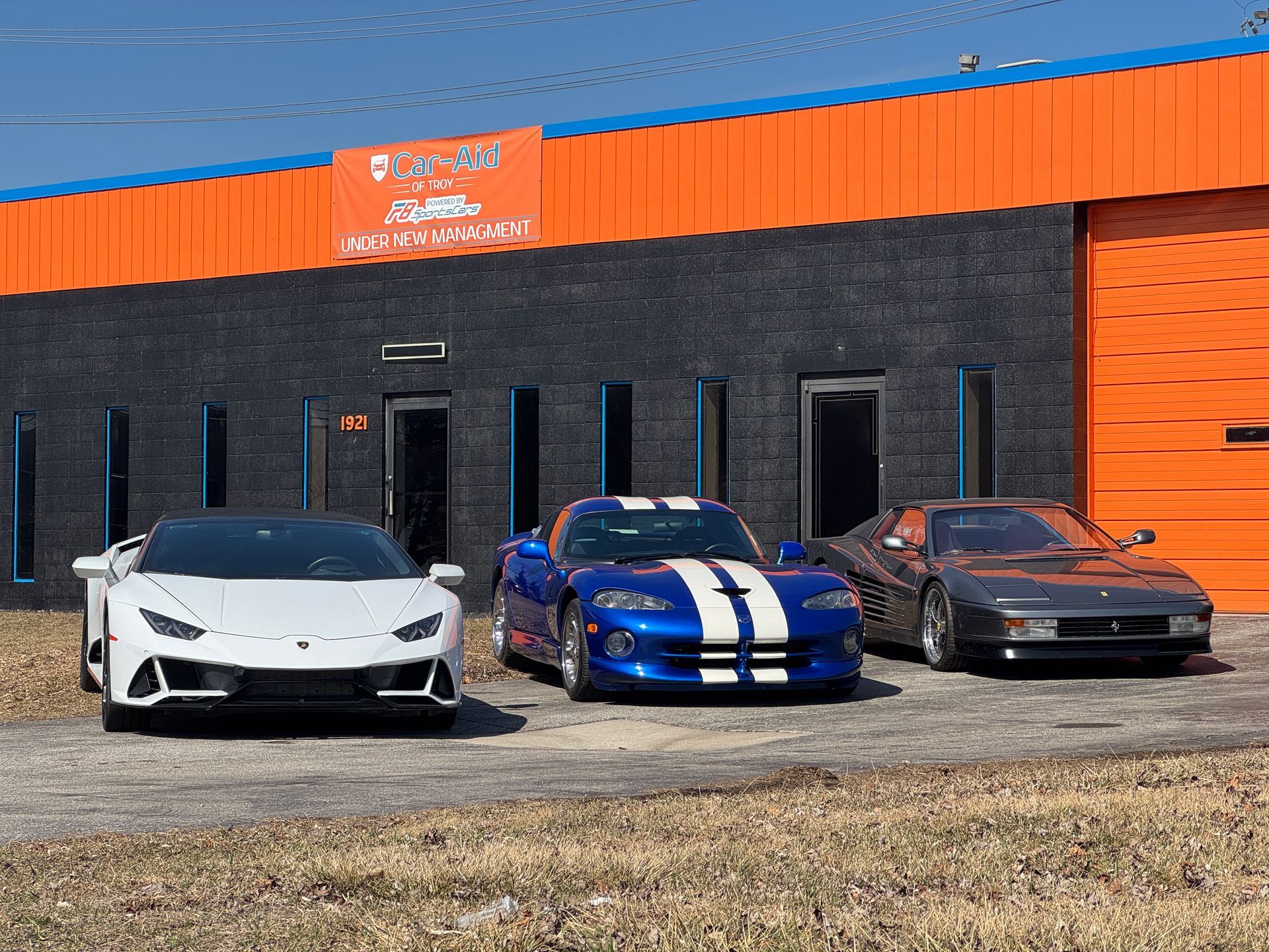 Three sports cars are parked in front of an orange building.