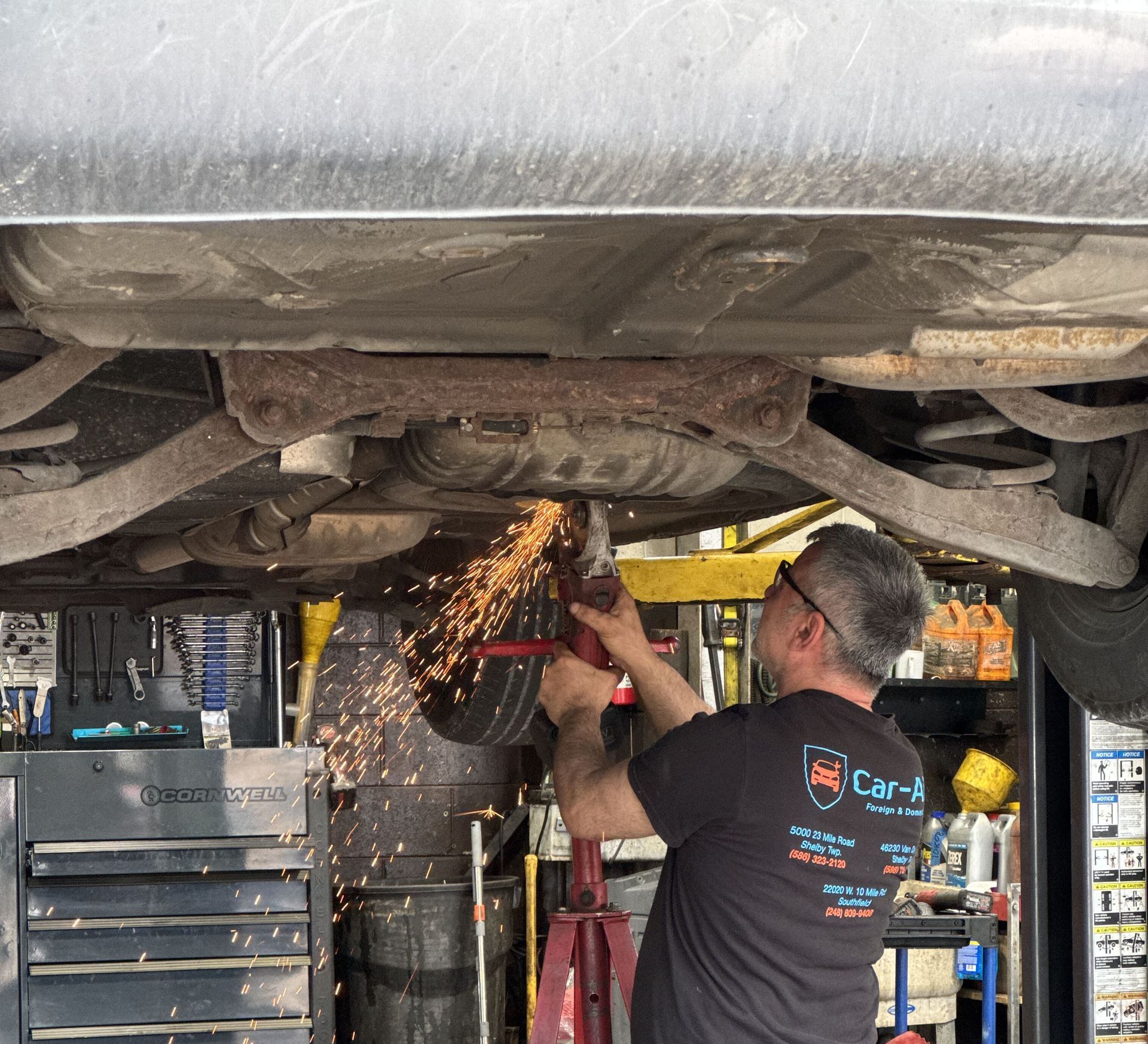 A car is being repaired in a garage with the hood up.