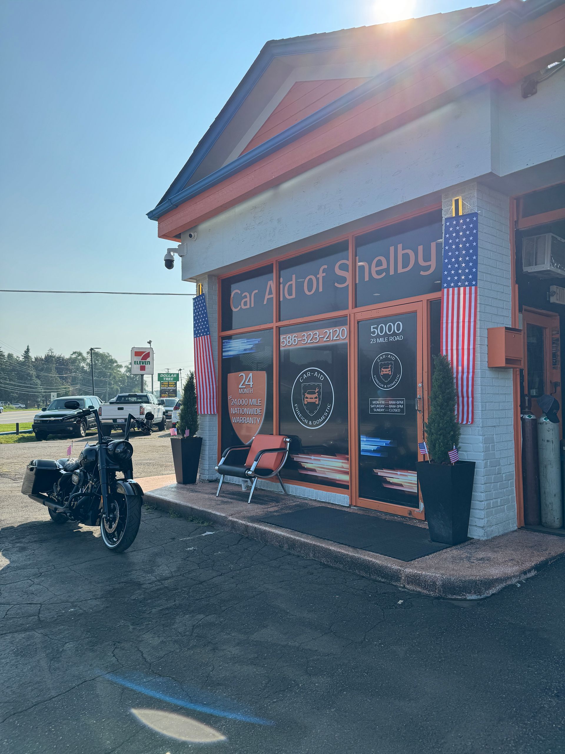 Car Aid of Shelby storefront with American flags. A black motorcycle is parked in front.