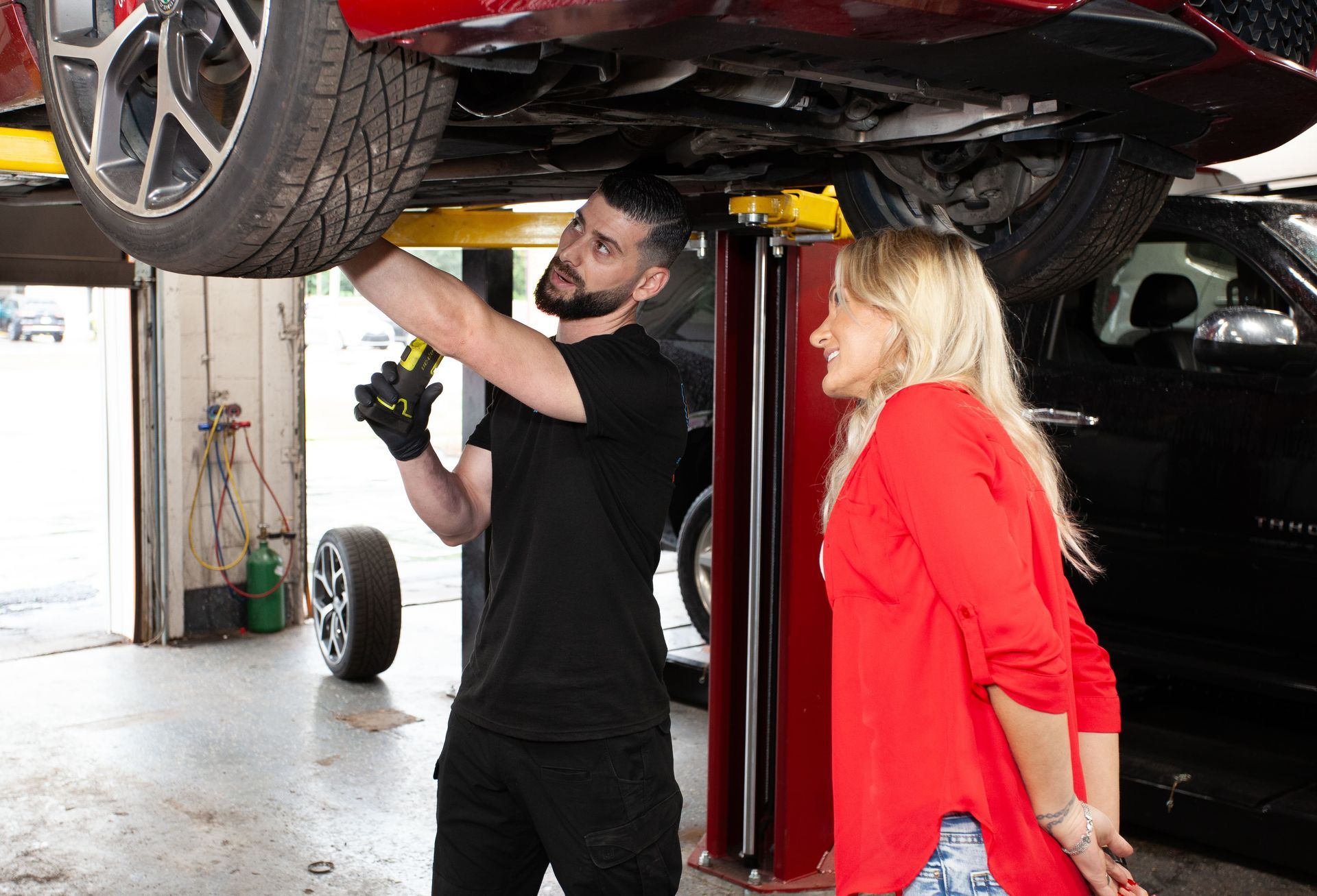 A man and a woman are looking under a car in a garage.