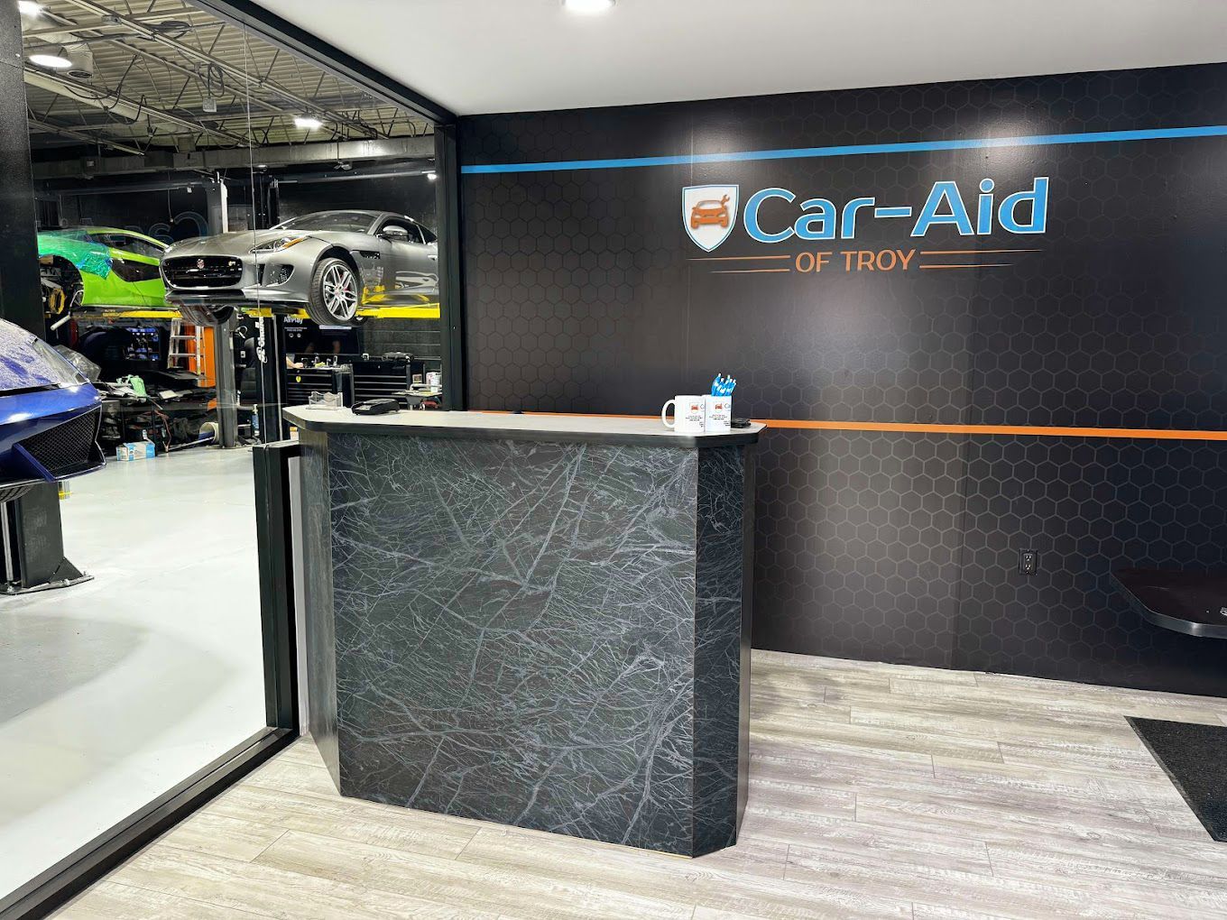 Reception area of a car repair shop with a counter, logo, and partially visible car lifts and cars.