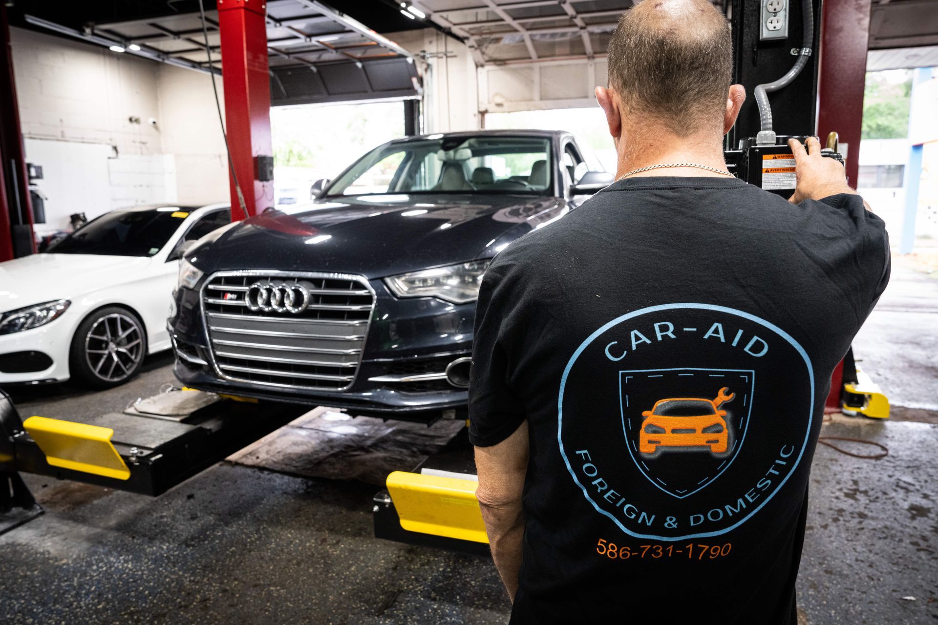 Mechanic pointing at dark Audi on lift in a garage, with 