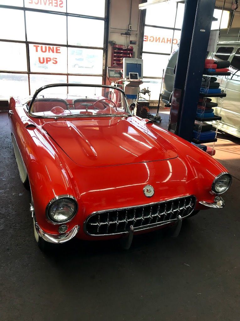 A red car is parked in a garage next to a sign that says tune ups.