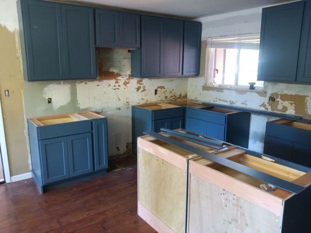 A kitchen under construction with blue cabinets and wooden drawers