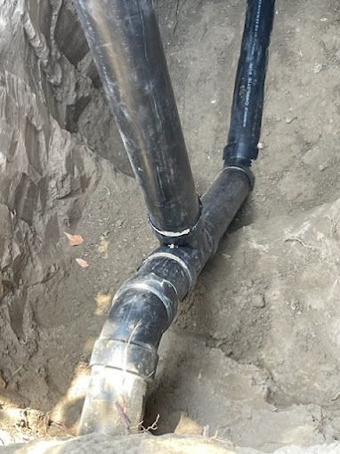 Two black pipes are connected to each other in the dirt.