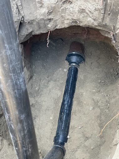 A black pipe is coming out of a hole in the ground.