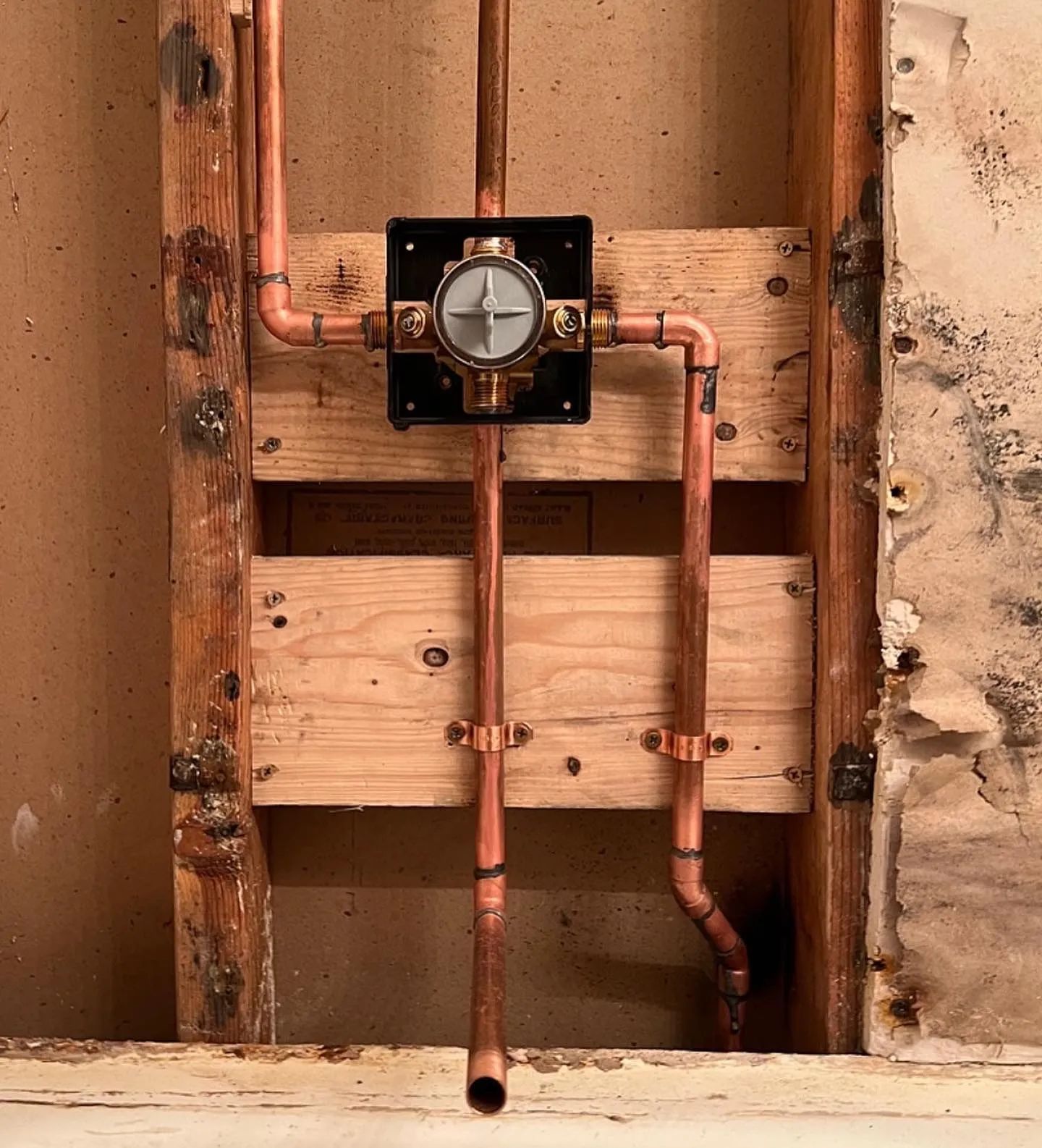 Copper plumbing for a shower valve, mounted on wooden framing.